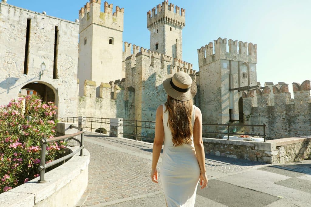 Travel in Italy. Back view of tourist woman walking in Sirmione towards the Scaligero Castle. Rear view of girl enjoying visiting Europe.